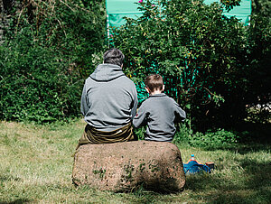 Vater und Sohn auf Baum sitzend, von hinten fotografiert.