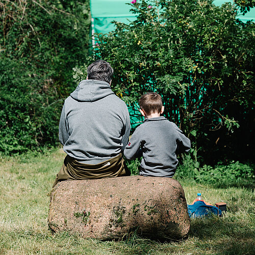 Vater und Sohn auf Baum sitzend, von hinten fotografiert.