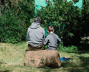 Vater und Sohn auf Baum sitzend, von hinten fotografiert.